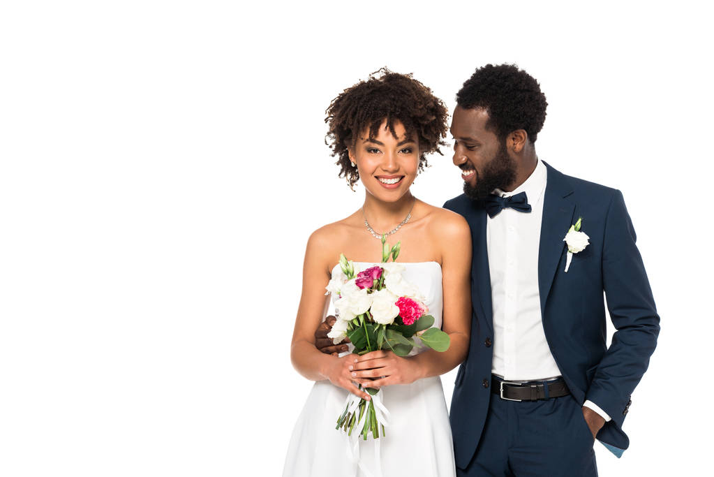 Happy african american bride holding bouquet near bridegroom